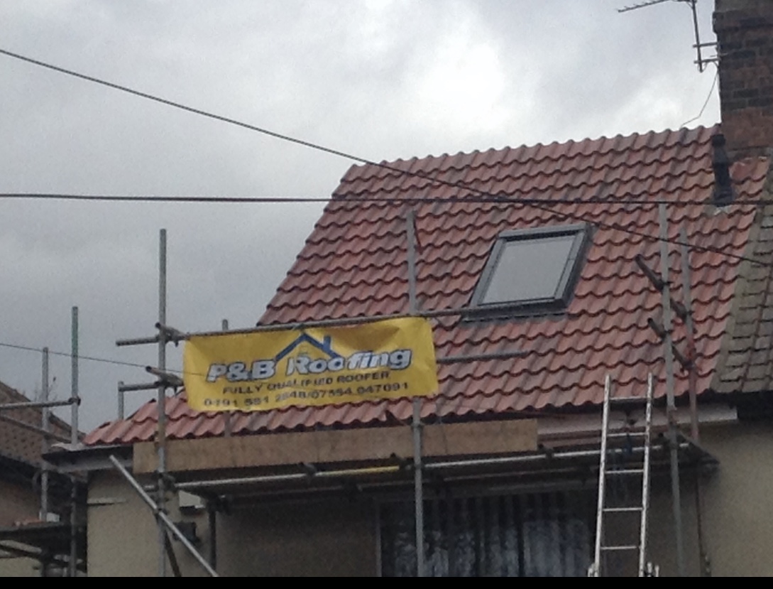 A new red tiled roof with a Velux window, with the yellow P&B Roofing banner on the scaffold
